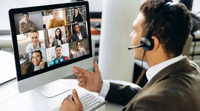 Business professional in a headset joining a video conference with colleagues on a computer screen.