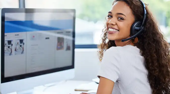 Smiling woman with a headset working on a desktop computer.